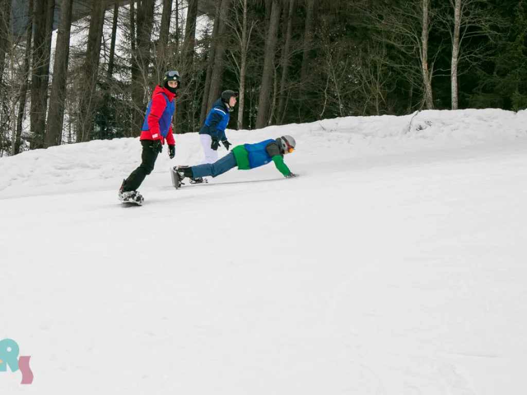 Snowboarder am Hang, daneben eine liegende Person.
